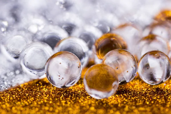 Hydrogel water balls on gold and silver glitter texture surface. Close up of gel ball.