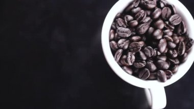 Koyu kahve çekirdekleri beyaz fincan siyah yüzey üzerinde döndürme.