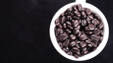 Koyu kahve çekirdekleri beyaz fincan siyah yüzey üzerinde döndürme.