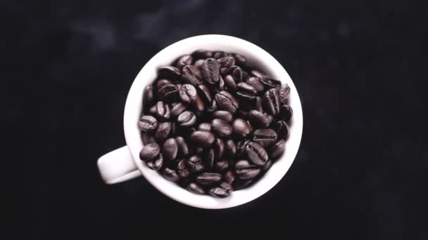 Темные Кофейные Зёрна Белой Чашке Вращаются Черной Поверхности — стоковое видео