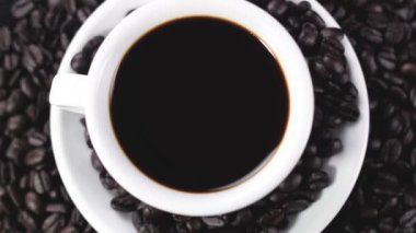 Kahve çekirdekleri karanlık yüzey üzerinde dönen ile plaka üzerinde beyaz fincan sade kahve. Yakın çekim.