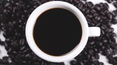 Kahve çekirdekleri beyaz yüzey üzerinde dönen ile beyaz fincan sade kahve. Yakın çekim.