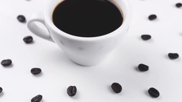 Чёрный Кофе Белой Чашке Кофейными Зернами Вращающимися Белой Поверхности Закрыть — стоковое видео
