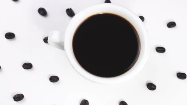 Μαύρο Καφέ Στο Λευκό Φλυτζάνι Κόκκους Καφέ Περιστρεφόμενες Λευκή Επιφάνεια — Αρχείο Βίντεο