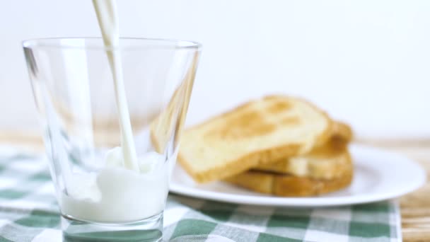 牛乳が白いプレートにトーストとグリーンのテーブル クロス木製キッチン表面のガラスを注ぐします スローモーション映像 — ストック動画