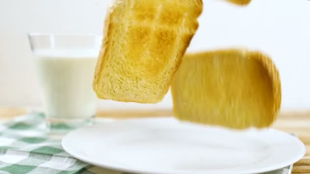 木製キッチンの面のガラスにミルクで白い皿の上に落ちてパンをトーストします スローモーション映像 — ストック動画