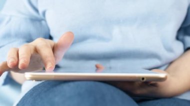 Kadın kanepede beyaz ve altın tableti kullanır. Yavaş çekim 4k görüntüleri yakın çekim.