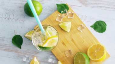 Narenciye, buz ve mavi ahşap mutfak masasında içme tüpü ile taze kokteyl kapatın. Limon ve limon. Yakından kapatın. Yaz içkisi. 4k.