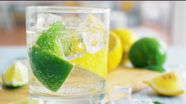 Buz küpleri ve kabarcıklar su ile cam dilimlenmiş limon ve kireç. Narenciye ile yaz kokteyli. 4k yakın çekim.