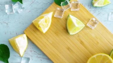 Ahşap mutfak yüzeyinde dilimlenmiş kireç ve limon kapatın. Ahşap doku yüzeyinde buz küpleri ile taze narenciye. 4k.