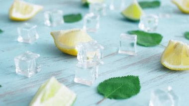 Mavi ahşap doku yüzeyinde buz küpleri ve yeşil yaprakları ile taze dilimlenmiş kireç ve limon kapatın. Mutfakta 4k narenciye.