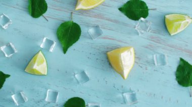 Mavi ahşap doku yüzeyinde buz küpleri ve yeşil yaprakları ile taze dilimlenmiş kireç ve limon kapatın. Mutfakta 4k narenciye. Üstte görüntü.