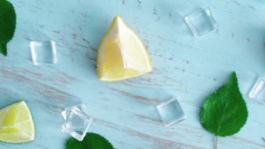 Mavi ahşap doku yüzeyinde buz küpleri ve yeşil yaprakları ile taze dilimlenmiş kireç ve limon kapatın. Mutfakta 4k narenciye. Üstte görüntü.