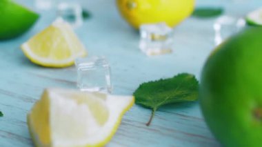 Mavi ahşap doku yüzeyinde buz küpleri ve yeşil yaprakları ile taze dilimlenmiş kireç ve limon kapatın. Mutfakta 4k narenciye.