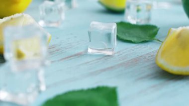 Mavi ahşap doku yüzeyinde buz küpleri ve yeşil yaprakları ile taze dilimlenmiş kireç ve limon kapatın. Mutfakta 4k narenciye.