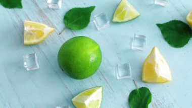 Mavi ahşap doku yüzeyinde buz küpleri ve yeşil yaprakları ile taze dilimlenmiş kireç ve limon kapatın. Mutfakta 4k narenciye. Üstte görüntü.