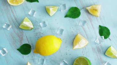 Mavi ahşap doku yüzeyinde buz küpleri ve yeşil yaprakları ile taze dilimlenmiş kireç ve limon kapatın. Mutfakta 4k narenciye. Üstte görüntü.