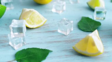 Mavi ahşap doku yüzeyinde buz küpleri ve yeşil yaprakları ile taze dilimlenmiş kireç ve limon kapatın. Mutfakta 4k narenciye.