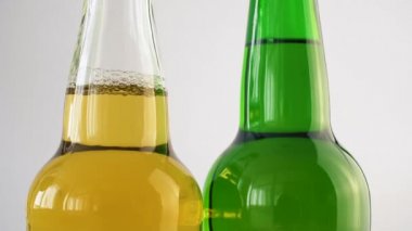 Beyaz izole arka planda dönen iki şişe bira. Şeffaf ve yeşil şişelerde alkol olabilir 4k yakın.