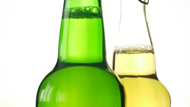 两瓶啤酒在白色隔离背景上旋转 特写可以酒精饮料在透明和绿色瓶 — 图库视频影像