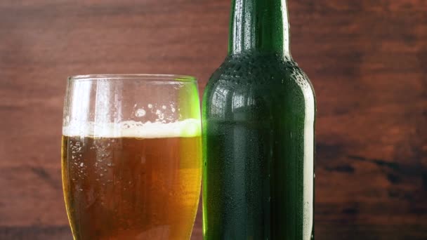 暗い質感の背景に回転するビールとガラスのボトルのクローズアップ 4Kフッテージ — ストック動画