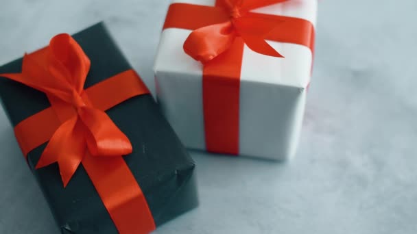 灰色のテクスチャ表面に回転する赤いシルクのリボンが付いている黒と白のギフトボックス クリスマス ブラックフライデー その他の休日のためのギフトボックス 4K映像をクローズアップ — ストック動画