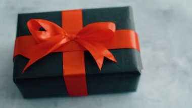 Doku yüzeyinde dönen kırmızı ipek kurdele ile siyah hediye kutusu. Noel, kara cuma ve diğer tatiller için hediye kutusu. 4k görüntüleri kapatın.
