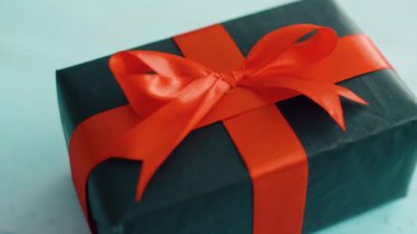 Mavi ahşap doku üzerinde dönen kırmızı ipek kurdele ile siyah hediye kutusu. Noel, kara cuma ve diğer tatiller için hediye kutusu. 4k görüntüleri kapatın.