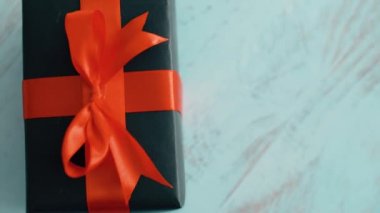 Mavi ahşap doku üzerinde dönen kırmızı ipek kurdele ile siyah hediye kutusu. Noel, kara cuma ve diğer tatiller için hediye kutusu. 4k görüntüleri kapatın.