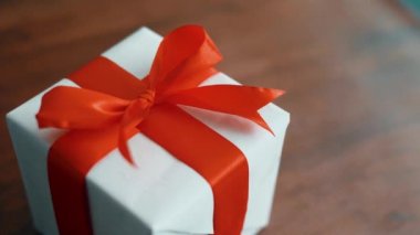 Ahşap doku yüzeyinde dönen kırmızı ipek kurdele ile beyaz hediye kutusu. Noel, kara cuma ve diğer tatiller için hediye kutusu. 4k görüntüleri kapatın.