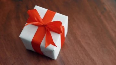 Ahşap doku yüzeyinde dönen kırmızı ipek kurdele ile beyaz hediye kutusu. Noel, kara cuma ve diğer tatiller için hediye kutusu. 4k görüntüleri kapatın.