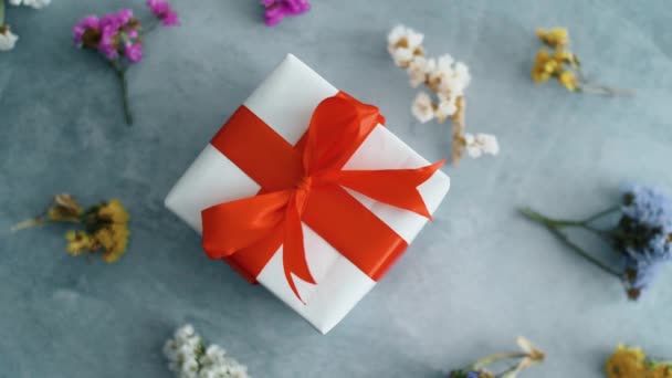 白色礼品盒 红色丝带在纹理表面旋转 带干色花 圣诞节 黑色星期五和其他节日的礼品盒 — 图库视频影像