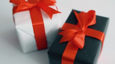 Beyaz arka plan üzerinde dönen kırmızı ipek kurdele ile siyah ve beyaz hediye kutusu. Noel, kara cuma ve diğer tatiller için hediye kutuları. 4k görüntüleri kapatın.