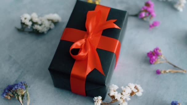 Чорна Подарункова Коробка Червоною Шовковою Стрічкою Обертається Поверхні Текстури Сухими — стокове відео