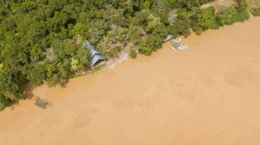 Kinabatangan nehrinin orman ağaçlarıyla çevrili bir kısmının ve tekneli küçük bir rıhtımın havadan görüntüsü.