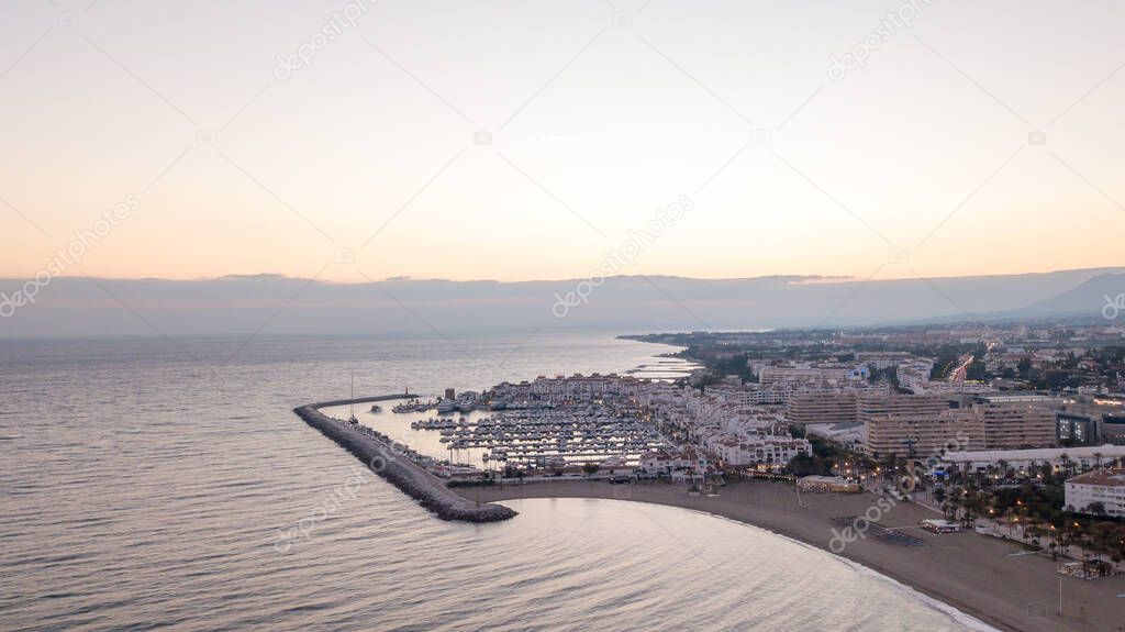 amazing sunset in puerto banus, marbella. orange and soft orange in the sky with a calm sea, and the light house in the scene