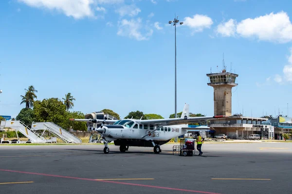 Zanzibar, 28 / 09 / 18. Zanzibar Uluslararası Havalimanı apronunda Cessna 208 Coastal Air karavan yerel havayolu park ve personel yükleme bagaj, kontrol kulesi ve terminal arka planda.