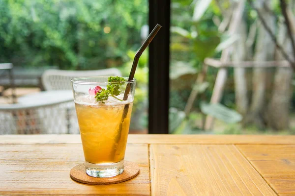 Buzlu taze gül çayı ve ahşap masanın üzerinde kurumuş güllerle dolu cam bardak..