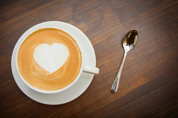 Ahşap masa arkasında beyaz bardakta sanat kalbi şekilli sıcak kahve. (Üst Görünüm)