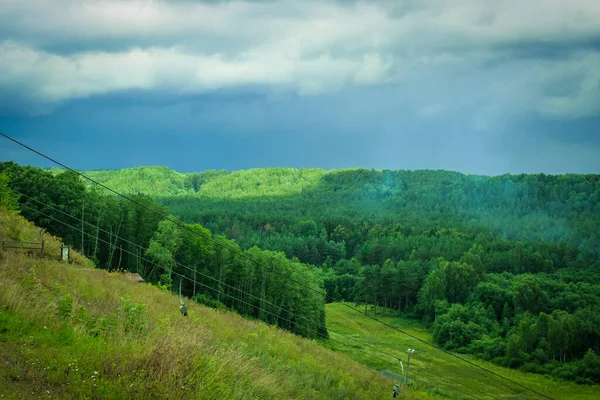 Dramatic landscape with thunder sky and green forest. Empty chairlift in ski resort . Ski resort in summer.