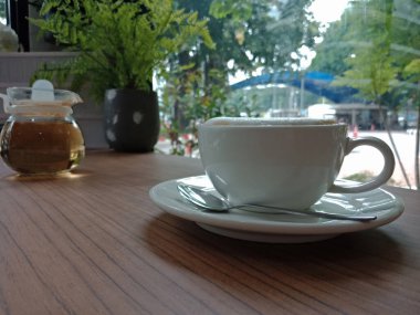 Beyaz bardakta kapuçino ve kahve dükkanındaki ahşap masaya konmuş sıcak çay.