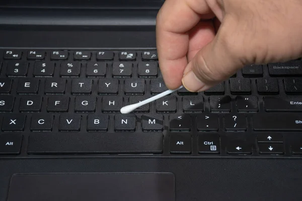 The right hand holds a cotton swab to clean the laptop\'s keyboard.