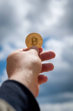 mavi gökyüzü arka plan üzerinde elinde altın sikke bitcoin