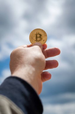 mavi gökyüzü arka plan üzerinde elinde altın sikke bitcoin