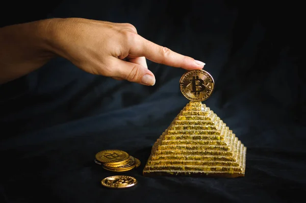 bir parmak bir altın sikke bitcoin piramidin tepesinde tutar