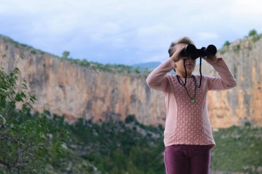 Dağın arka planında dürbünü olan kız.