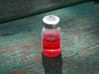 Eski yeşil bir masada kırmızı ilaç şişesi.