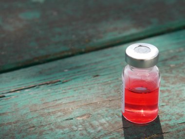 Eski yeşil bir masada kırmızı ilaç şişesi.