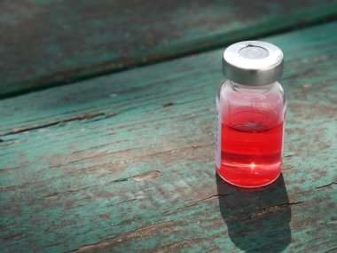 Eski yeşil bir masada kırmızı ilaç şişesi.