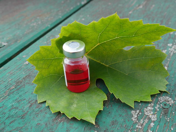 Красная бутылка с лекарством на фоне листа на старом столе 